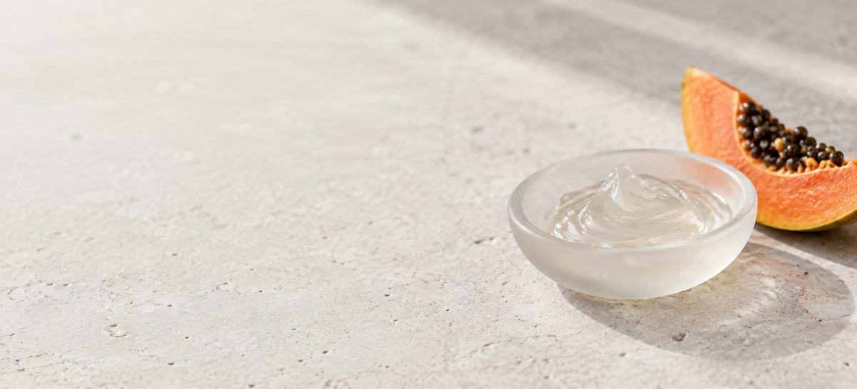 Translucent skincare gel in a frosted dish beside a papaya slice.