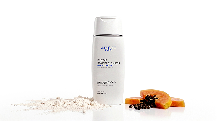 Ariège Paris Enzyme Powder Cleanser bottle on a white background, styled with a pile of white powder, papaya slices, and black pepper on a reflective white surface.