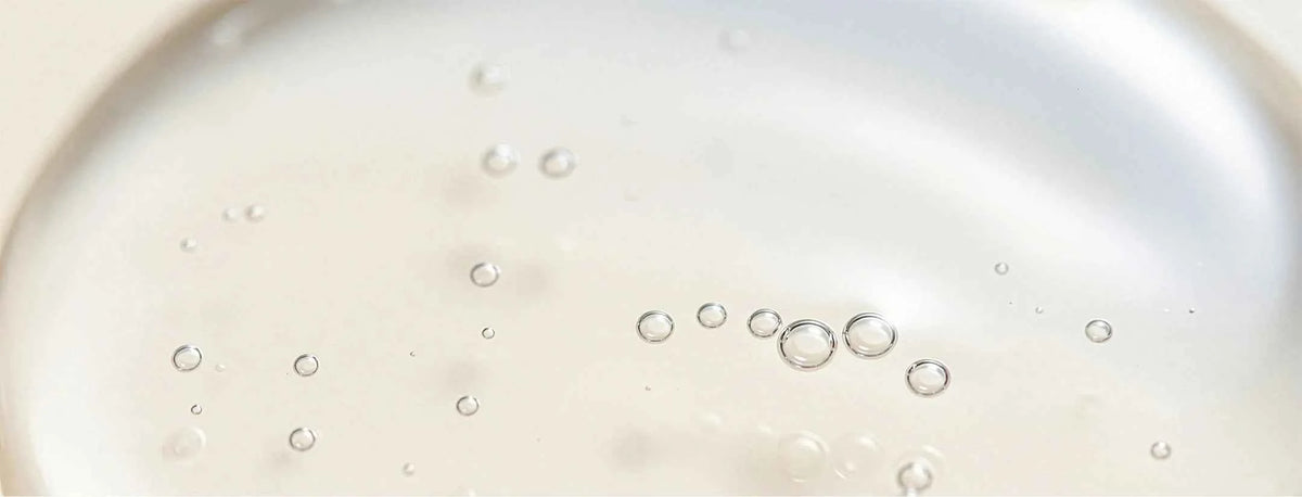 A close-up of a translucent, glossy, off-white liquid with small clear bubbles floating on the surface.