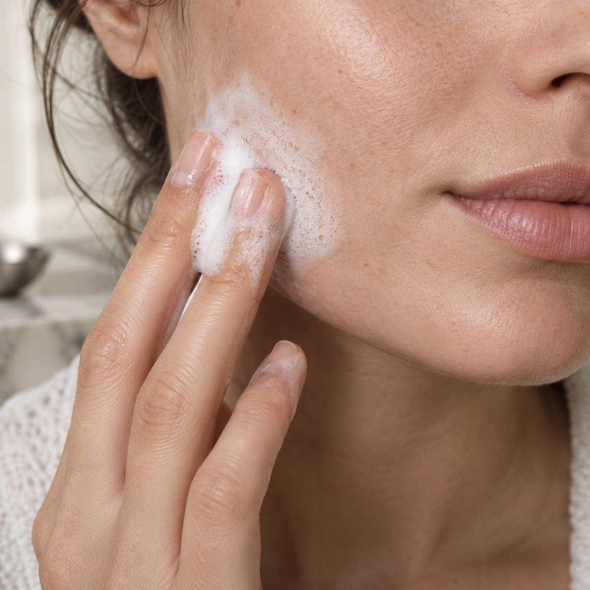 Fingertips gently applying cleansing foam to the lower cheek.