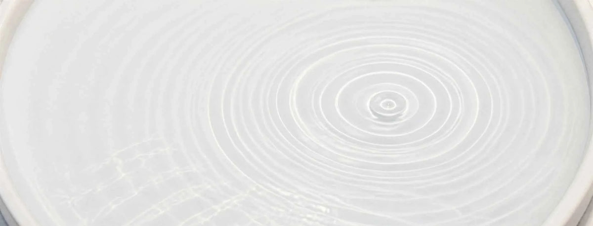 A close-up of a white circular surface with concentric ripples radiating from a central point, resembling water in motion.