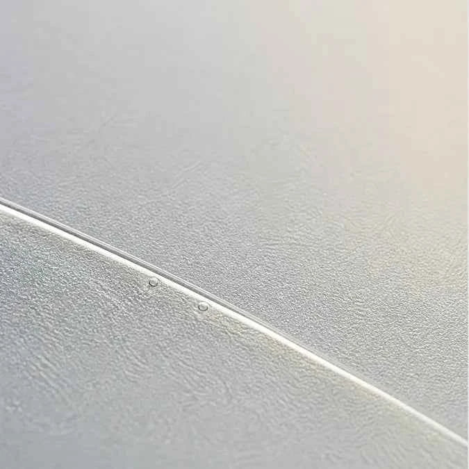 A close-up of a frosted, textured surface with a diagonal seam or edge, showing a subtle sheen and small water droplets.