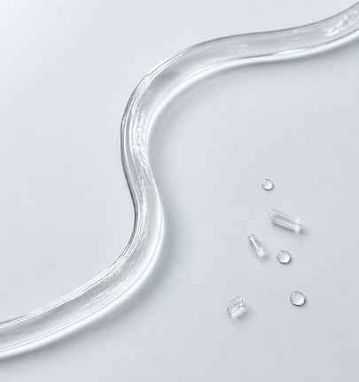 A close-up of a translucent clear silicone or rubber tube curving across a light gray surface, with a few small clear cylindrical and circular pieces scattered nearby.