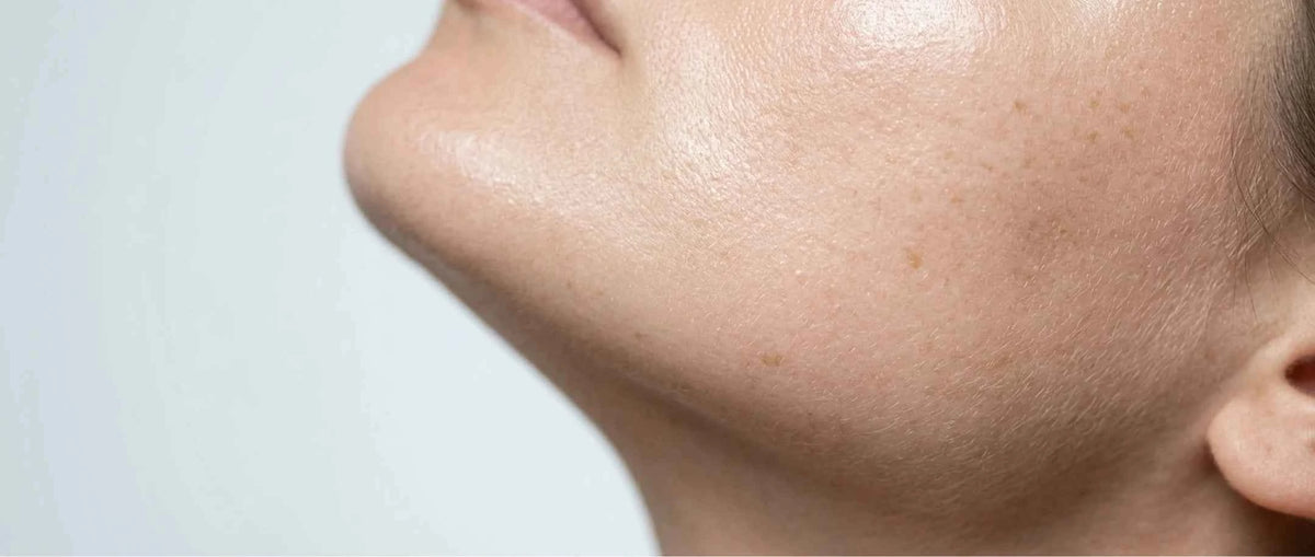 Close-up of a person's lower face and neck showing smooth, clear skin against a light gray background.