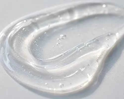 A close-up of a translucent, clear gel or silicone pad with a wavy, curved shape and small water droplets on its surface, set against a light gray background.