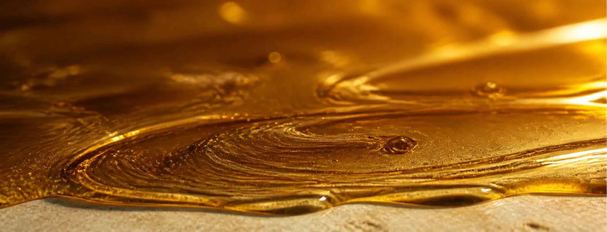 A close-up of glossy golden amber liquid with swirling textures and reflective highlights over a light surface.