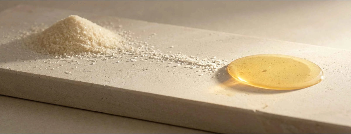 A close-up of a beige stone slab with a small pile of white powder on one side and a glossy pool of golden-yellow liquid on the other, lit by warm directional sunlight.
